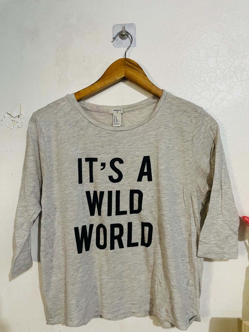 Forever 21 Shirt (Category: Tshirts & Polo Shirts ) located in San Mateo. Submitted by safeearth21 (Listing ID 1467589808, Image 2). Description: - Brand: Forever 21 - Design: Light grey marled knit with bold black 'IT'S A WILD WORLD' graphic - Sleeves: Three-quarter length - Neckline: Classic round neck - Size: Medium (tag attached) - Material: Soft and comfortable - Condition: Great casual wear.