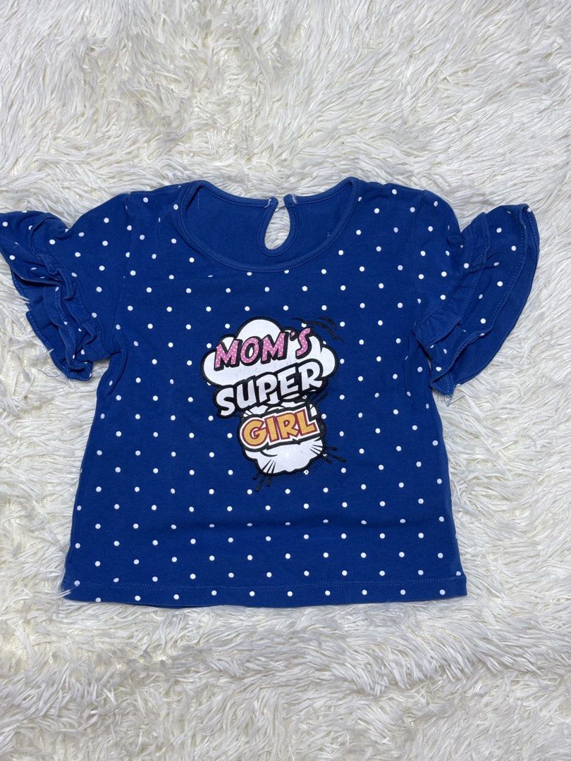 girl top (Category: Babies & Kids Fashion) located in Dagupan City. Submitted by iamrannflores (Listing ID 1467409895, Image 1). Description: - Brand/Size: justees baby, Size 24 Months - Design: Blue with white polka dots and 'MOM'S SUPER GIRL' graphic in the center - Details: Short flutter sleeves with ruffled edges and back button closure - Material/Care: Machine wash cold (instructions printed inside) - Condition: Excellent, like new - Perfect