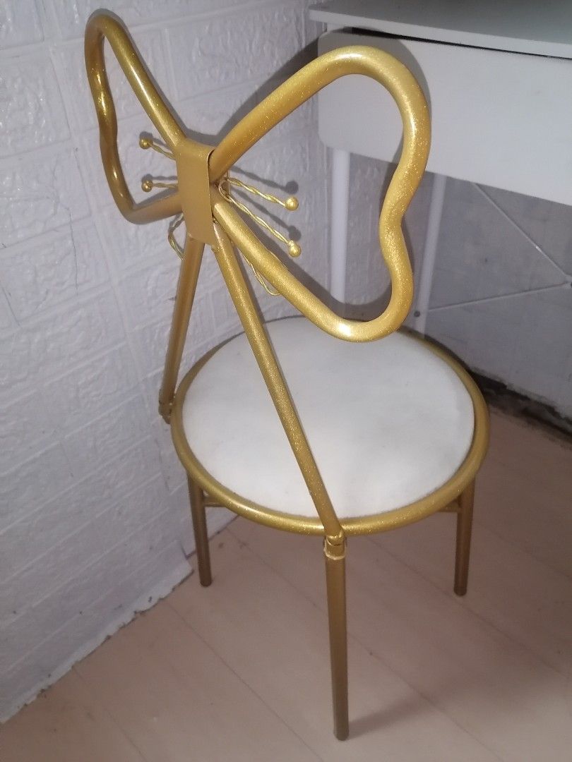 Gold Bow Back Vanity Chair White Cushion (Category: Chairs) located in Manila. Submitted by yzekielshop (Listing ID 1467390688, Image 2). Description: - Gold metal frame with a gorgeous glitter finish - Unique bow-shaped backrest with wire knot details - Comfortable round seat with white upholstery - Sleek and sturdy slim cylindrical legs - Compact size, ideal for makeup desks and vanity spaces.