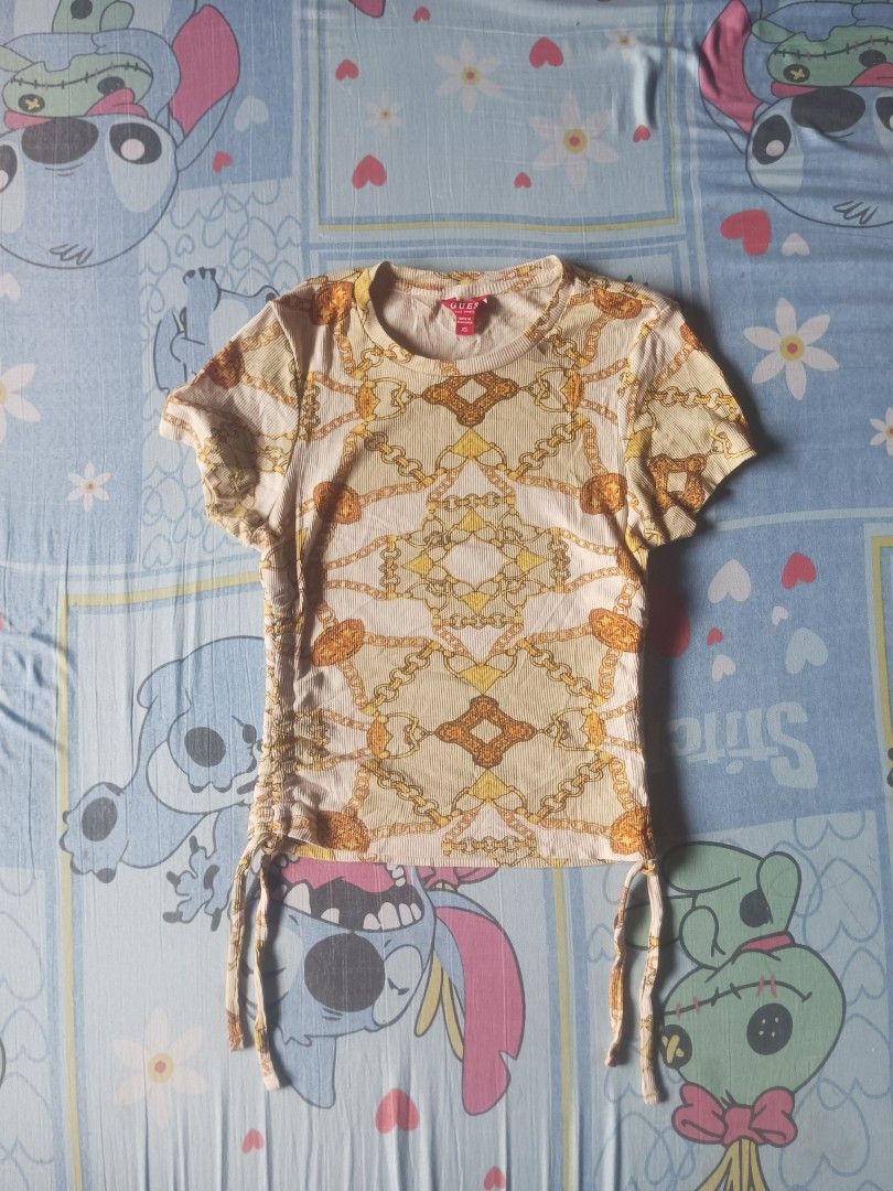 GUESS Kardy Ruched Top (Category: Shirts) located in San Pablo. Submitted by halloweenxx (Listing ID 1467435959, Image 1). Description: - Brand: GUESS - Size: XS - Color/Design: Cream and yellow with all-over ornate gold chain baroque pattern - Fit & Features: Short sleeves, round neckline, and side drawstrings to adjust length and fit - Material: Ribbed fabric - Origin: Made in Bangladesh - Condition: Excellent XS - S/Semi Med.