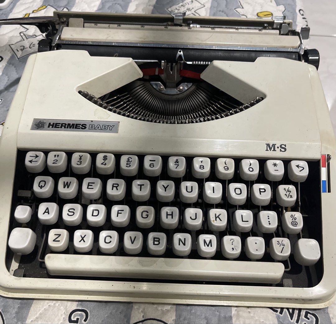Hermes Baby M-S Typewriter with Hard Case (Category: Stationery & School Supplies) located in Cagayan de Oro. Submitted by brex7 (Listing ID 1467469720, Image 3). Description: - Vintage Hermes Baby M-S manual typewriter in classic white - Compact and portable design featuring a standard QWERTY layout - Includes original textured beige hard carrying case - Fully mechanical with ribbon spools inside - Minor dust and cosmetic wear from previous use 