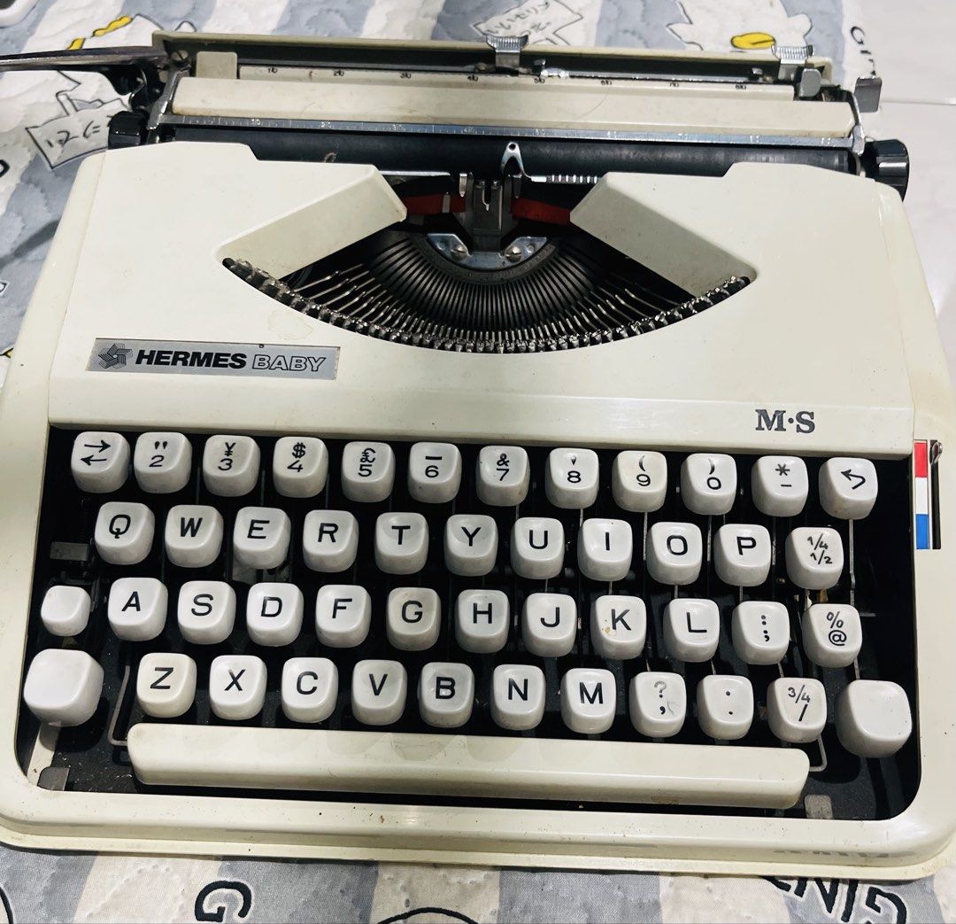 Hermes Baby M-S Typewriter with Hard Case (Category: Stationery & School Supplies) located in Cagayan de Oro. Submitted by brex7 (Listing ID 1467469720, Image 1). Description: - Vintage Hermes Baby M-S manual typewriter in classic white - Compact and portable design featuring a standard QWERTY layout - Includes original textured beige hard carrying case - Fully mechanical with ribbon spools inside - Minor dust and cosmetic wear from previous use 