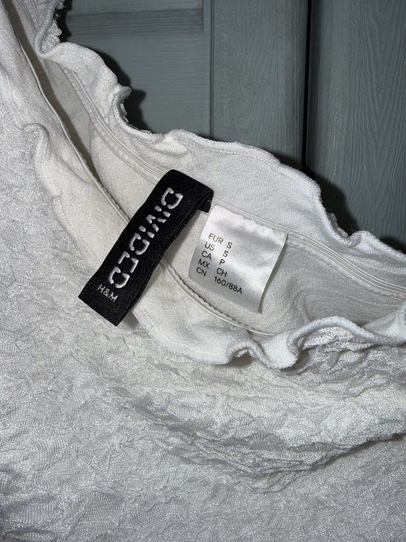 H&M Divided White One-Shoulder Textured Top Size S (Category: Sleeveless) located in Manila. Submitted by aprilled (Listing ID 1467493841, Image 2). Description: - Brand: H&M Divided - Style: One-shoulder top with ruffled neckline trim - Fabric: Textured crinkled fabric - Size: S (fits true to size) - Color: White - Condition: Pre-loved with a couple of small yellowish stains near the front lower section and middle, still lots of wear left.