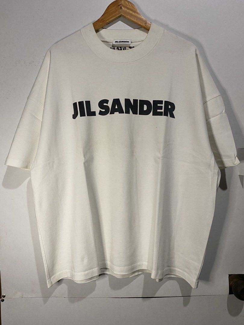 JIL SANDER TSHIRT (Category: Tshirts & Polo Shirts ) located in Jaen. Submitted by oshimamark58418 (Listing ID 1467536853, Image 1). Description: - Brand: Jil Sander - Color: White with bold black logo print - Size: XXL (Width: 24", Length: 27") - Style: Oversized / Casual streetwear - Condition: Excellent, well-maintained.