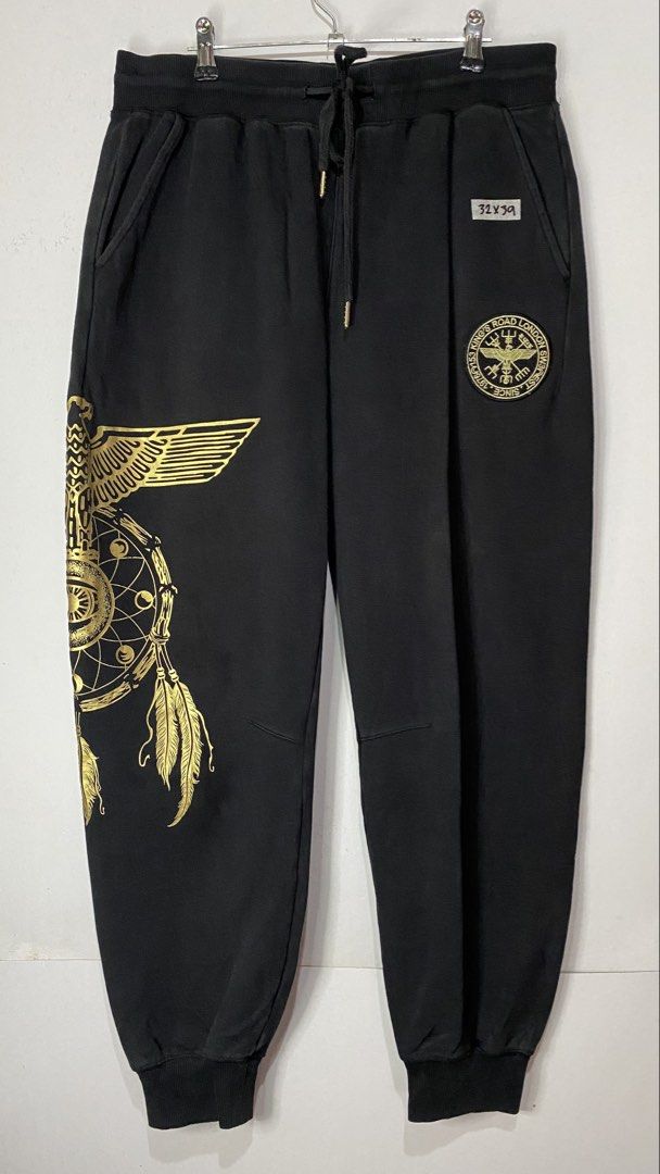 JOGGER PANTS (Category: Joggers) located in Jaen. Submitted by oshimamark58418 (Listing ID 1467409833, Image 1). Description: - Brand: Boy London - Style: Jogger Pants / Sweatpants - Color: Black with metallic gold prints - Size: 32 (Medium) - Features: Bold gold eagle & dreamcatcher graphic on leg, front badge logo, and 'BOY' embroidery on back pocket - Details: Elastic waistband with drawstring, rib-knit cuffs - Condition: Excellent pre-owned c