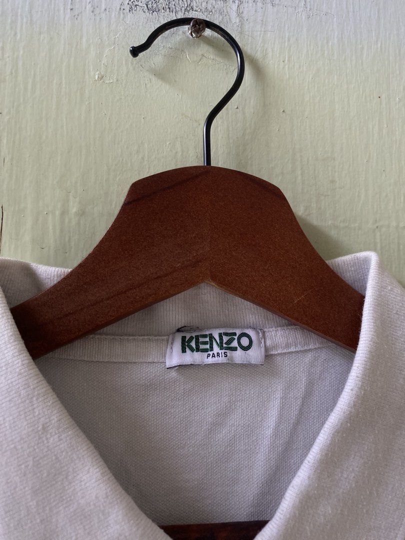 Kenzo Paris White Polo Shirt (Category: Tshirts & Polo Shirts ) located in Pandi. Submitted by nasya_thrift_collection2023 (Listing ID 1467413700, Image 2). Description: - Brand: Kenzo Paris - Color: White - Material: Premium cotton pique fabric - Design: Classic collar with three-button placket, short sleeves - Details: Small black logo patch on left chest, ribbed collar and cuffs - Condition: Excellent, clean neckline label - Shipping: Ships vi