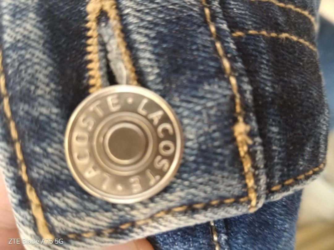 Lacoste Denim Jeans (Category: Jeans) located in Malabon City. Submitted by jullie_bag_shop (Listing ID 1467510878, Image 2). Description: Authentic Lacoste denim jeans in medium blue wash. Classic five-pocket design featuring the embroidered crocodile logo on the back pocket. Branded metal button closure and leather waistband patch embossed with Lacoste lettering. Internal pocket lining printed with brand logo and size 34. Sturdy stitching and t