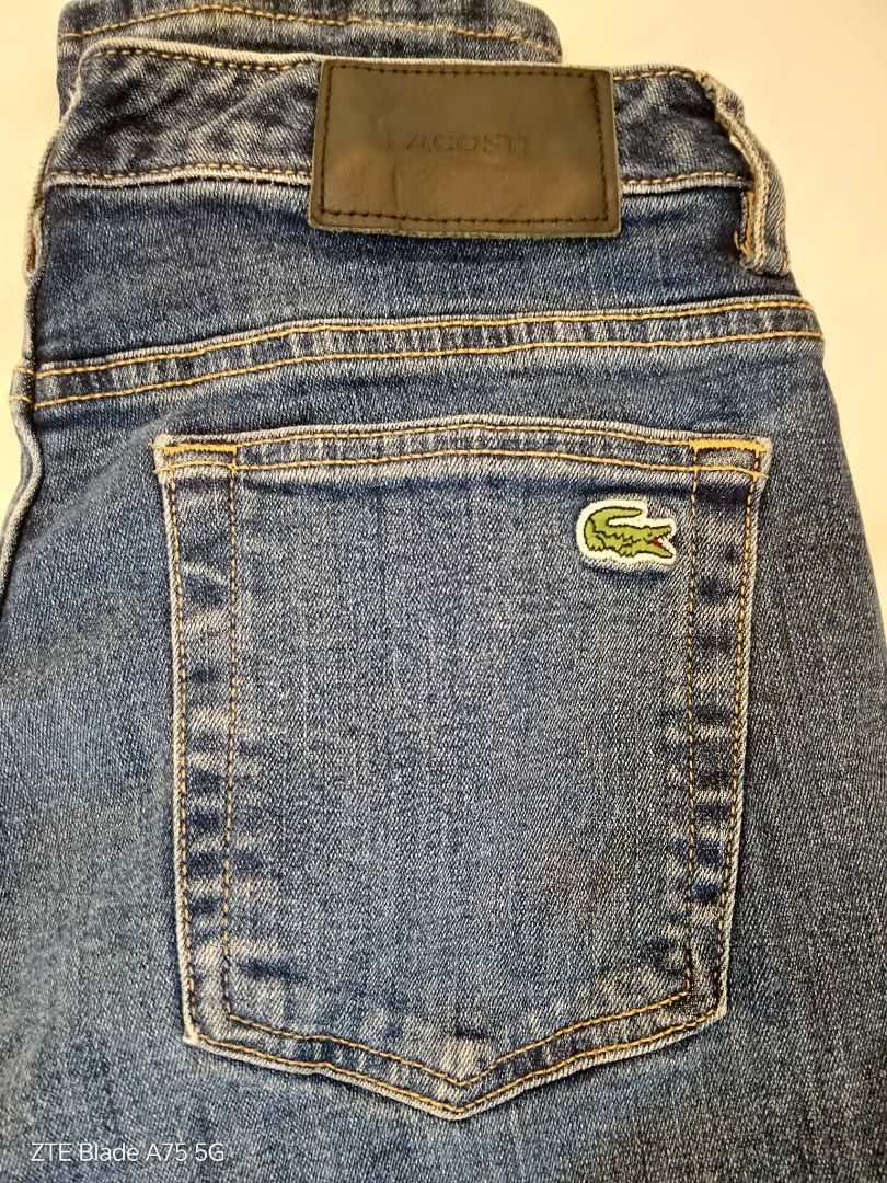Lacoste Denim Jeans (Category: Jeans) located in Malabon City. Submitted by jullie_bag_shop (Listing ID 1467510878, Image 1). Description: Authentic Lacoste denim jeans in medium blue wash. Classic five-pocket design featuring the embroidered crocodile logo on the back pocket. Branded metal button closure and leather waistband patch embossed with Lacoste lettering. Internal pocket lining printed with brand logo and size 34. Sturdy stitching and t