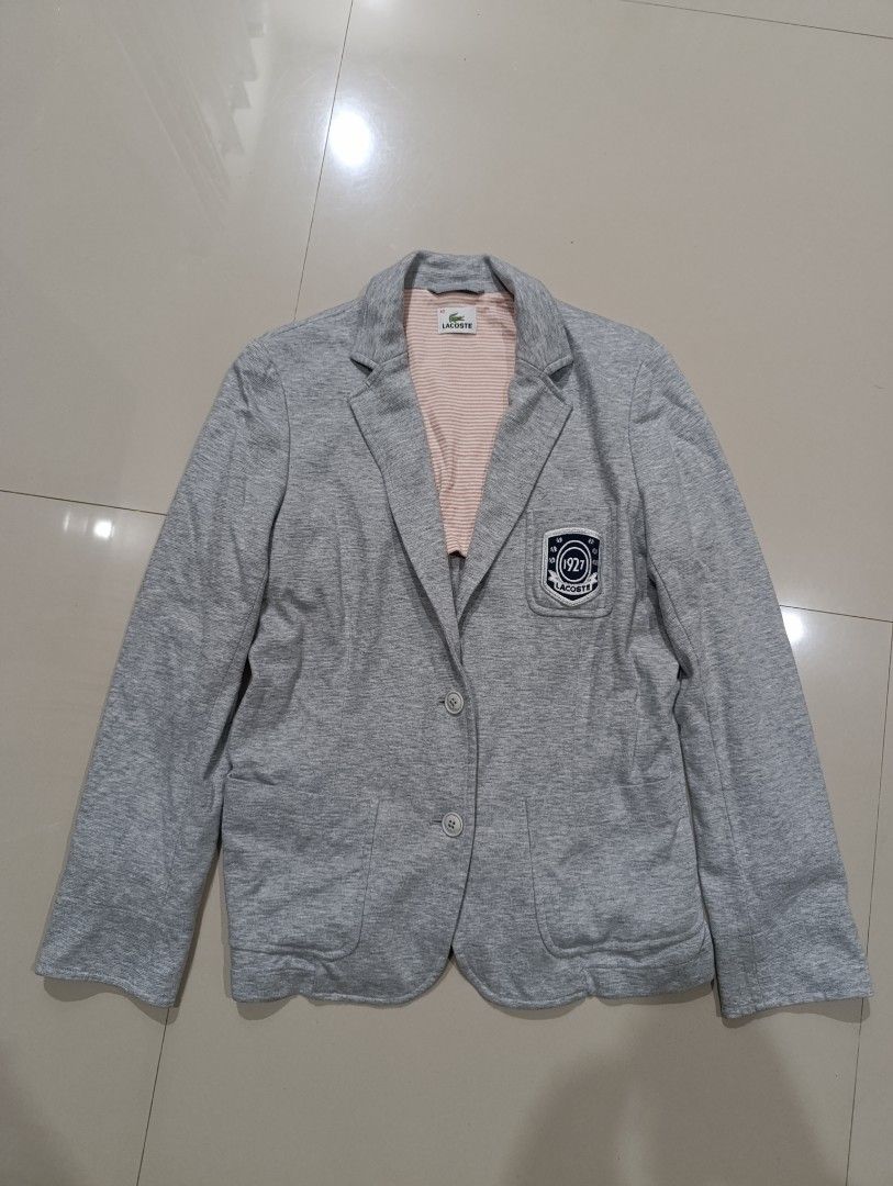 Lacoste Grey Blazer Jacket Size 42 (Category: Coats, Jackets and Outerwear) located in Davao. Submitted by idioticthrifter (Listing ID 1467546758, Image 1). Description: - Brand: Lacoste - Size: 42 - Color: Grey with pink and white striped inner lining - Material: Cotton outer, polyester sleeve lining - Details: Two front buttons, front pockets, and '1927 Lacoste' embroidered crest patch on chest - Origin: Japanese care label inside - Condition: 