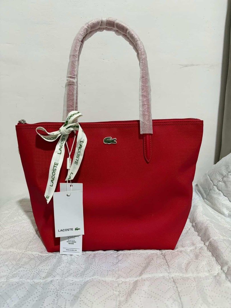 Lacoste Red Tote Bag With Ribbon Accent (Category: Tote Bags) located in Polomolok. Submitted by legadad94559 (Listing ID 1467566016, Image 2). Description: - Authentic Lacoste tote bag in a vibrant red canvas - Brand new with original retail tags attached - Secure top zipper closure - Sturdy shoulder straps still wrapped in protective plastic - Elegant branded ribbon tied neatly on the front handle - Spacious interior featuring a zippered pocket