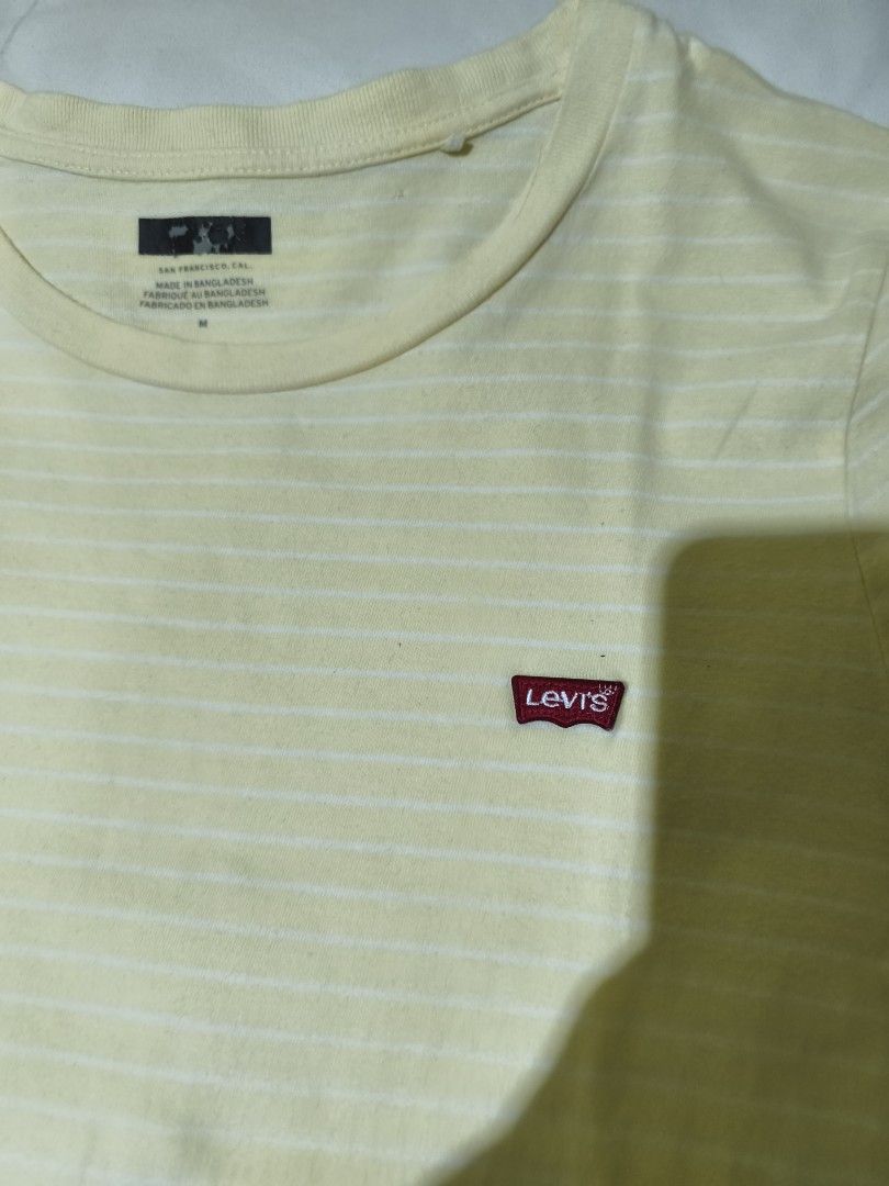 Levi's Yellow Striped T-Shirt (Category: Shirts) located in Quezon City. Submitted by tintinarms (Listing ID 1467521884, Image 2). Description: - Brand: Levi's - Style: Short sleeve crew neck tee with all-over white stripes - Color: Light yellow - Size: Medium (Made in Bangladesh) - Measurement: ~18 inches pit to pit (flat lay) - Details: Small red Levi's logo patch on the chest, soft and clean cotton fabric - Condition: Great casual basic for ev