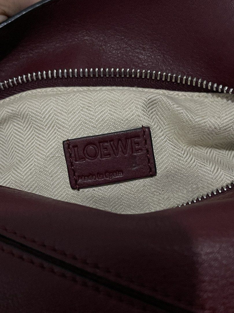 Loewe Puzzle Bag Burgundy Leather (Category: Luxury Bags & Wallets) located in Cavite. Submitted by cheetozjalapeeeeno (Listing ID 1467476271, Image 2). Description: Burgundy Loewe Puzzle bag in classic calfskin. Geometric panel design with silver-tone hardware. Removable shoulder strap with Anagram dice detail. Top handle and rear zip pocket. Cream herringbone canvas lining inside. Interior leather tag stamped Loewe Made in Spain. Structured sha