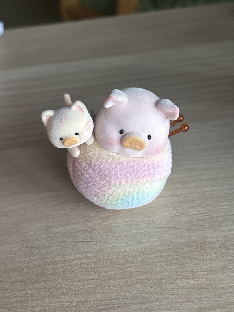 Lulu the Pig (Category: Designer & Blind Box Toys) located in Quezon City. Submitted by shopfinesse (Listing ID 1467397784, Image 1). Description: - Adorable flocked figurine set with a large pink pig and tiny white kitten - Animals are sitting together on a pastel rainbow ball of yarn with knitting needles - Features a smooth, soft velvety texture - Perfect as cute desk decor or shelf ornament.