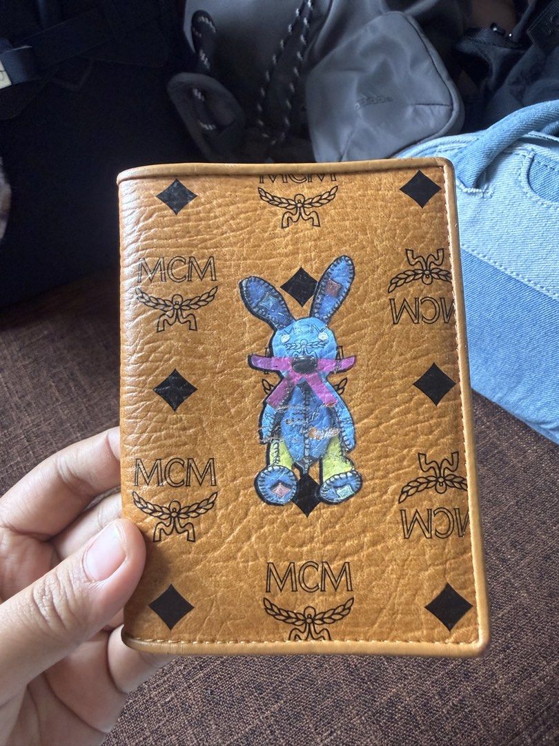 MCM Visetos Rabbit Passport Holder in Cognac. (Category: Luxury Bags & Wallets) located in Bayombong. Submitted by nica7 (Listing ID 1467369344, Image 3). Description: In good condition MCM Visetos Rabbit Passport Holder in Cognac. Product Details • Material: Coated canvas with Visetos monogram and leather trim • Color: Cognac brown exterior with a bright yellow/gold interior • Design Feature: Cartoon blue rabbit graphic printed on the front • In