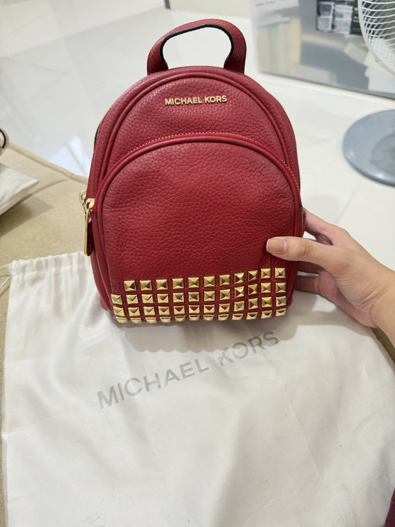 Michael Kors Red Studded Leather Mini Backpack (Category: Backpacks) located in Manila. Submitted by ktyyycloset (Listing ID 1467556823, Image 1). Description: - Brand: Michael Kors - Material: Premium pebbled leather in a bold red color - Hardware: Gold-tone throughout with chic pyramid studs on the bottom front - Compartments: Dual zipper closure, front zip pocket for extra storage - Handles: Sturdy top handle and adjustable shoulder straps - I