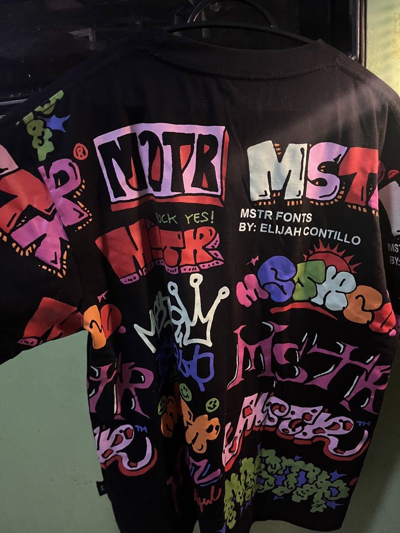 MSTR Fonts by Elijah Contillo Graphic Tee Black XL (Category: Tshirts & Polo Shirts ) located in Manila. Submitted by erlyn17 (Listing ID 1467479209, Image 3). Description: - Brand/Designer: Elijah Contillo x MSTR Fonts - Size: XL - Color: Black with vibrant multicolour graffiti text - Style: Heavy street-style aesthetic with all-over prints (front, back, and sleeves) - Details: Branded neck tape and unique graphic collar tag.