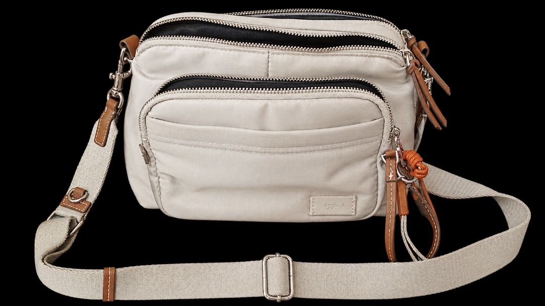 Neutral Crossbody Bag with Adjustable Strap and Multiple Pockets (Category: Cross-body Bags) located in Quezon City. Submitted by pyress (Listing ID 1467549473, Image 2). Description: - Color: Light grey with brown leather trim - Material: Durable fabric with adjustable canvas shoulder strap - Storage: Multiple zipped compartments inside and out for easy organizing - Design: Features a dark stripe strap accent and small rectangular logo patch - C