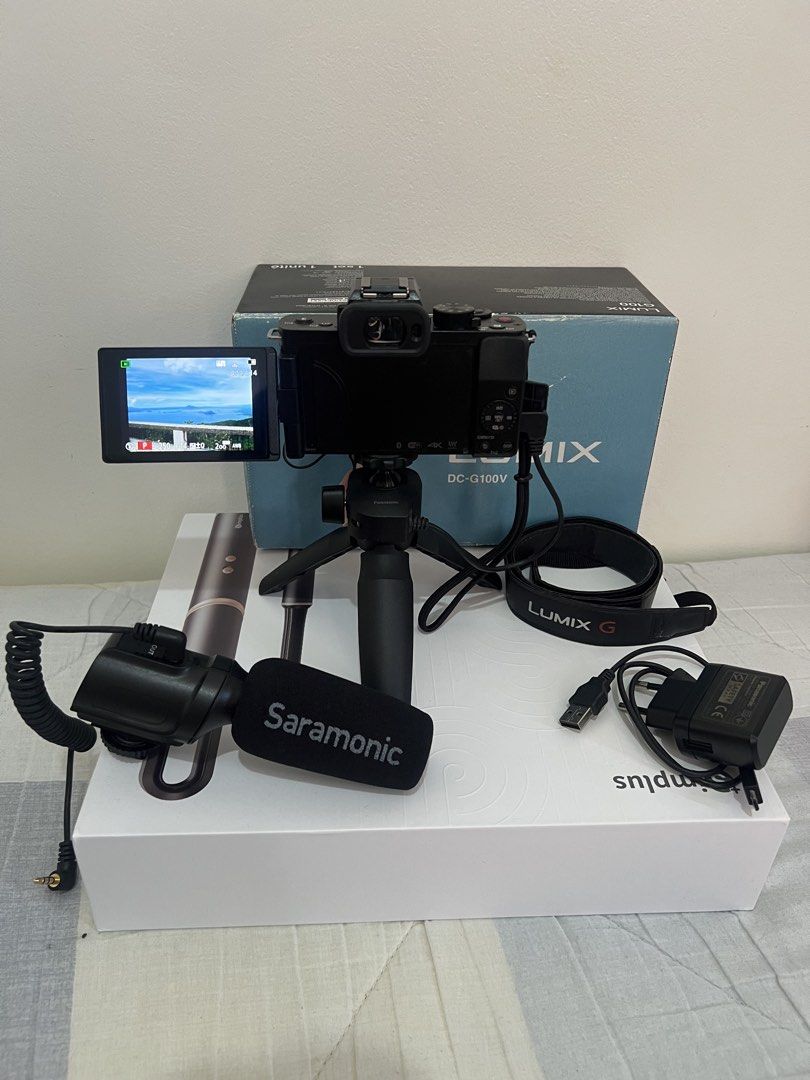 Panasonic Lumix G100V Mirrorless Camera Kit (Category: Cameras) located in San Jose del Monte. Submitted by joy_ochoa (Listing ID 1467403980, Image 2). Description: Panasonic Lumix DC-G100V mirrorless camera bundled with 12-32mm lens, tripod grip, Saramonic external microphone, strap, power adapter, and USB cable. Original box included. Fully operational with screen powered on. No issues. Bought from CameraHaus SM North for 44,000.