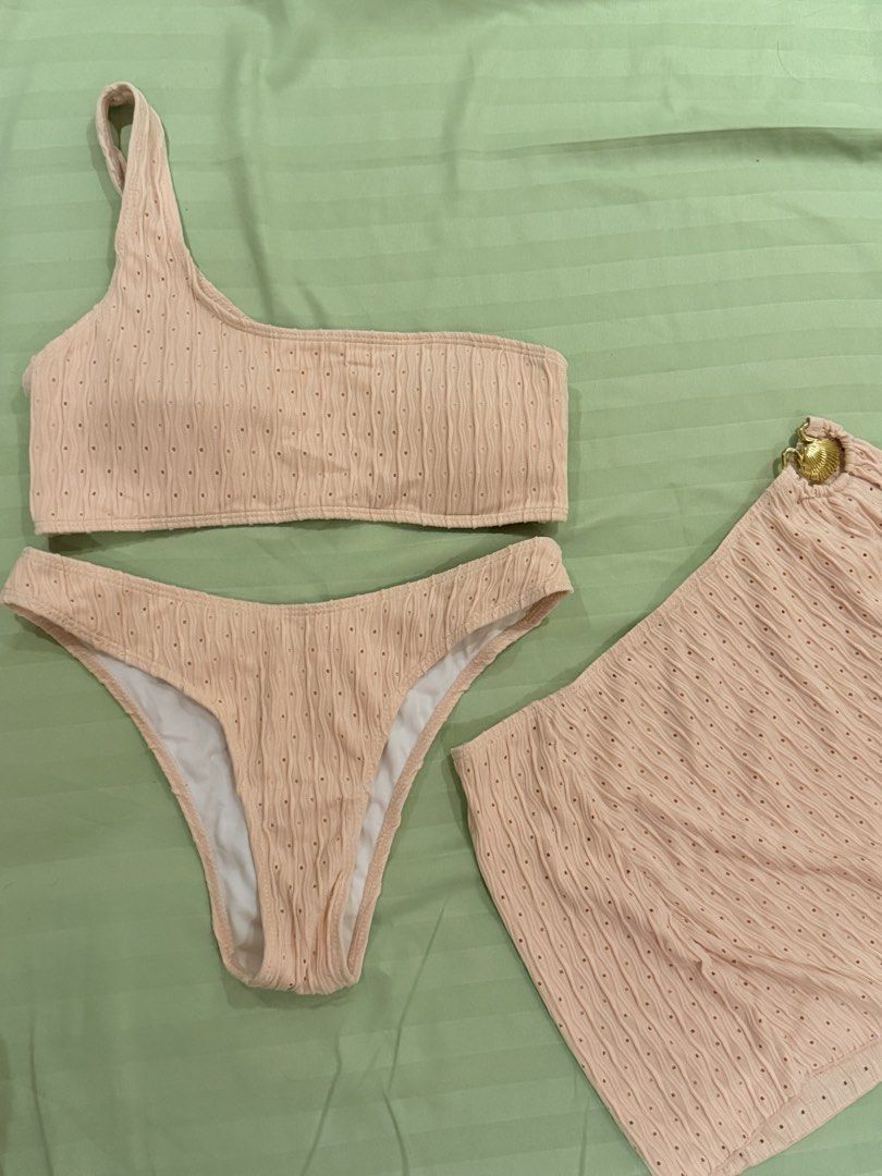 Pink Three-Piece One-Shoulder Bikini Set with Sarong (Category: Bikinis & Swimsuits) located in Quezon City. Submitted by caathhx_ (Listing ID 1467508945, Image 1). Description: - Condition: Brand new, never worn (hygiene sticker still attached) - Color: Pale pink - Material: Textured fabric with tiny eyelet details - Set includes: One-shoulder top, classic brief bottoms with white inner lining, and a matching wrap sarong skirt - Special detail: 