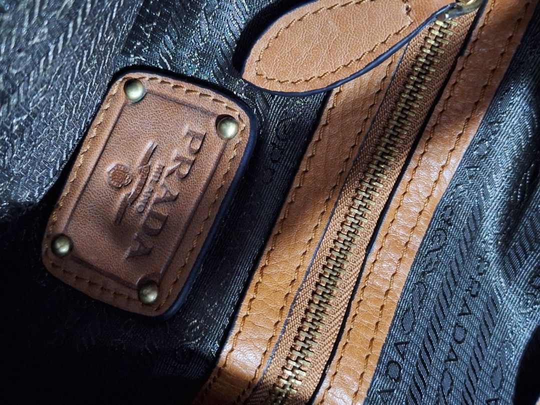 Prada Brown Leather Shoulder Bag (Category: Luxury Bags & Wallets) located in Quezon City. Submitted by cloudymay (Listing ID 1467518036, Image 2). Description: Prada shoulder bag in tan brown pebbled leather. Gold-tone hardware throughout. Structured top handle with adjustable strap details. Interior lined with Prada logo fabric, featuring a zippered pocket and embossed leather logo plaque. magnetic closure across the top. Shows slight leather d
