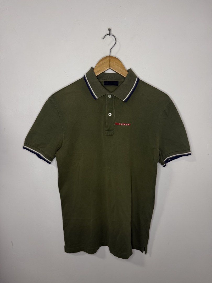 Prada Polo Shirt (Olive Green) (Category: Tshirts & Polo Shirts ) located in Manila. Submitted by jcarchives14 (Listing ID 1467443611, Image 1). Description: - Brand: Prada - Color: Olive green with white and blue contrast tipping on collar and cuffs - Details: Signature red Prada logo badge on left chest, two-button placket with white buttons - Style: Short sleeve, classic casual polo - Condition: Excellent pre-loved condition (Managed with care