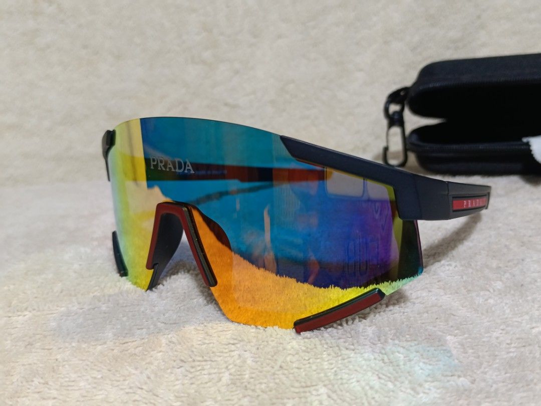 Prada Sport Sunglasses Shield Mirror Lens (Category: Sunglasses & Eyewear) located in Cavite. Submitted by navias (Listing ID 1467549878, Image 2). Description: - Brand: Prada - Model: 23053 - Design: Sporty wraparound shield sunglasses - Lenses: Multi-color mirrored with blue, green, and orange gradient tones - Frame: Matte black with striking red accents and iconic Prada logo on brow and temple - Inclusions: Original black hard case and cleanin
