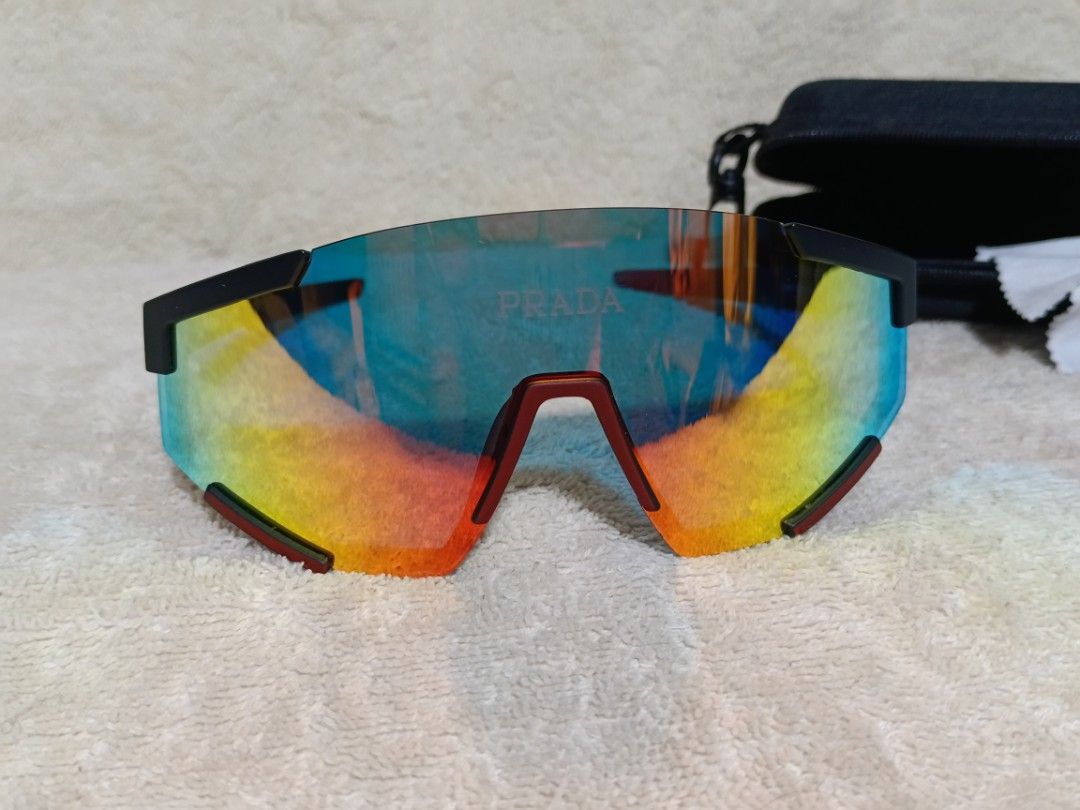 Prada Sport Sunglasses Shield Mirror Lens (Category: Sunglasses & Eyewear) located in Cavite. Submitted by navias (Listing ID 1467549878, Image 1). Description: - Brand: Prada - Model: 23053 - Design: Sporty wraparound shield sunglasses - Lenses: Multi-color mirrored with blue, green, and orange gradient tones - Frame: Matte black with striking red accents and iconic Prada logo on brow and temple - Inclusions: Original black hard case and cleanin