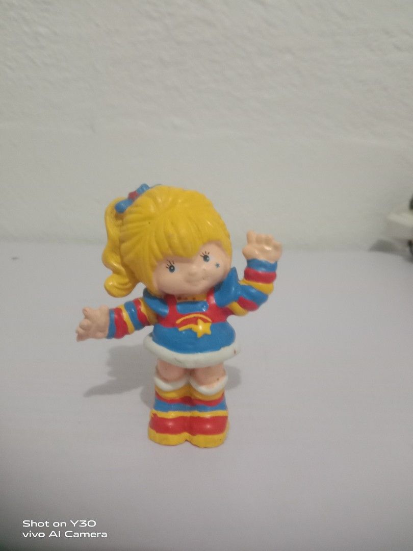Rainbow Brite (Category: Figurines & Statues) located in Orani. Submitted by rodel1991 (Listing ID 1467373897, Image 1). Description: - Retro plastic toy figure of a smiling blonde girl - Waving pose with one hand up - Colorful blue, red, and yellow outfit with striped sleeves and socks - Painted blue eyes and a cute star mark on the cheek - Bright primary color design, perfect for collectors.
