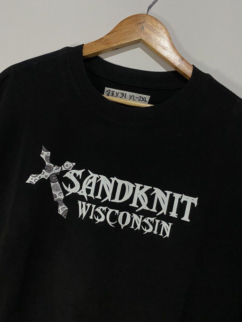 Sandknit Wisconsin Black Graphic Tee XXL (Category: Tshirts & Polo Shirts ) located in Jaen. Submitted by oshimamark58418 (Listing ID 1467550310, Image 3). Description: Black short-sleeve tee from Sandknit Wisconsin. Graphic print on the front and back featuring a dagger/cross motif with wings and text. 100 percent cotton material. Tag size XXL, measured approximately 23 by 31 inches. Wash care tag attached inside. Made in China..