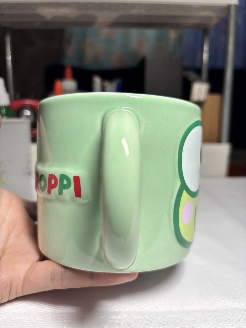 Sanrio Keroppi Ceramic Mug Paladone (Category: Coffee & Tea Tableware) located in Baguio. Submitted by 21enygrace.ph (Listing ID 1467480871, Image 2). Description: - Authentic Paladone x Sanrio Keroppi mug (2025 copyright) - Design: Big Keroppi face on front, spelled-out name pattern on back - Colors: Light green handle, white interior - Flaw: Small paint chip near the bottom rim - Care: Hand wash recommended (dishwasher and microwave unsafe).