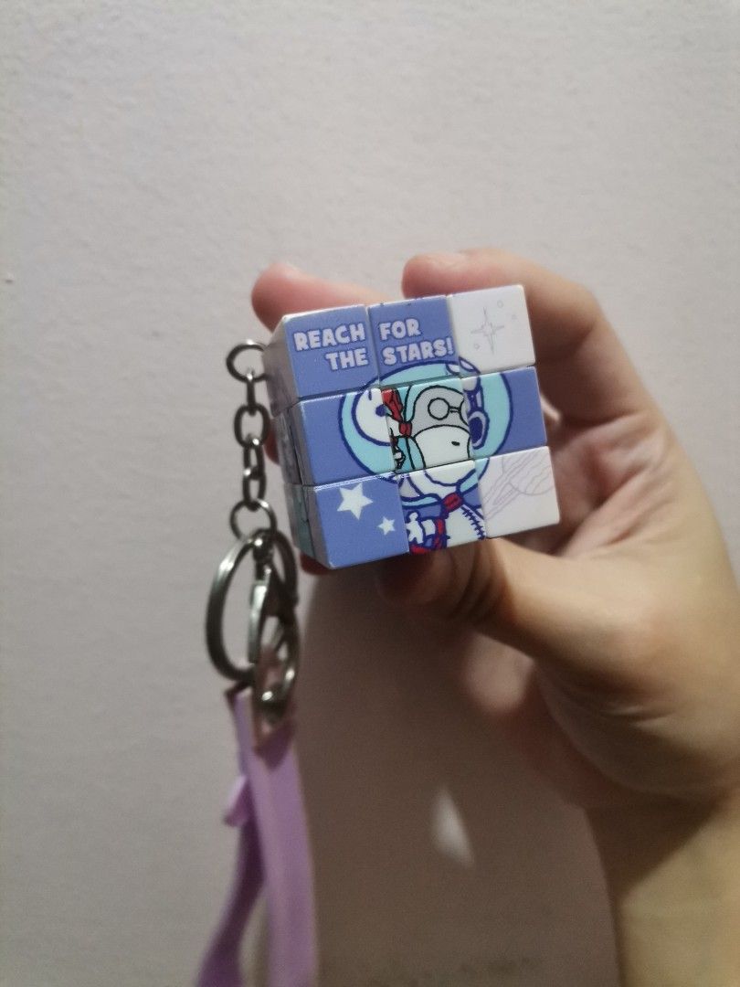 Snoopy Astronaut Rubik's Cube Keychain (Category: Character Goods) located in Makati City. Submitted by kookybearsstuff (Listing ID 1467495789, Image 2). Description: - Snoopy astronaut themed mini puzzle cube keychain - Functional mini puzzle cube with 'REACH FOR THE STARS!' print - Purple silicone wrist strap featuring 'SNOOPY' and planet designs - Durable silver metal keyring and chain attached - Fun and stylish accessory for keys, bags, or ba