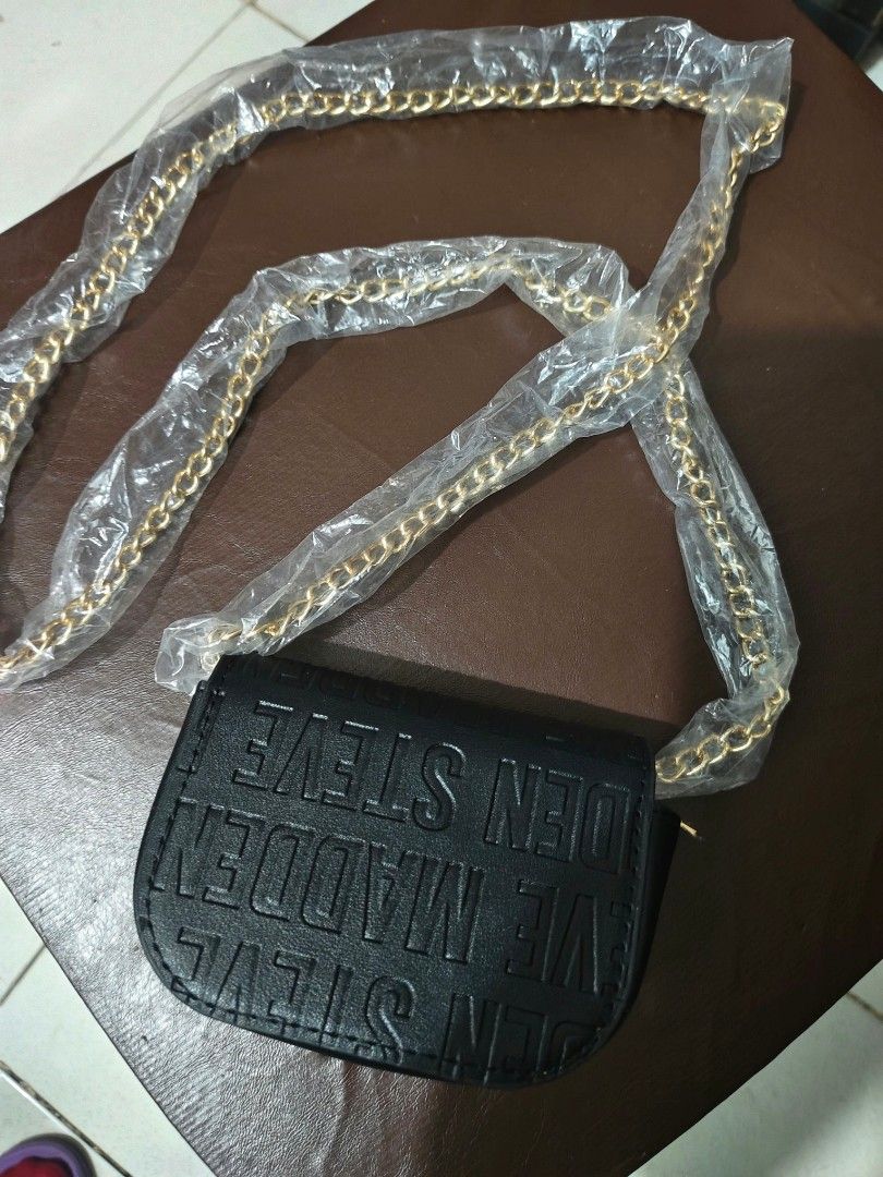 Steve Madden Black Crossbody Bag (Category: Cross-body Bags) located in Cavite. Submitted by mahthriftshop (Listing ID 1467382349, Image 3). Description: - Brand: Steve Madden - Color: Black with gold-tone hardware - Material: Faux leather with all-over embossed logo lettering - Strap: Gold-tone chain strap (still wrapped in original plastic) - Closure: Front flap with metallic Steve Madden logo plate - Interior: Includes a zipper compartment and