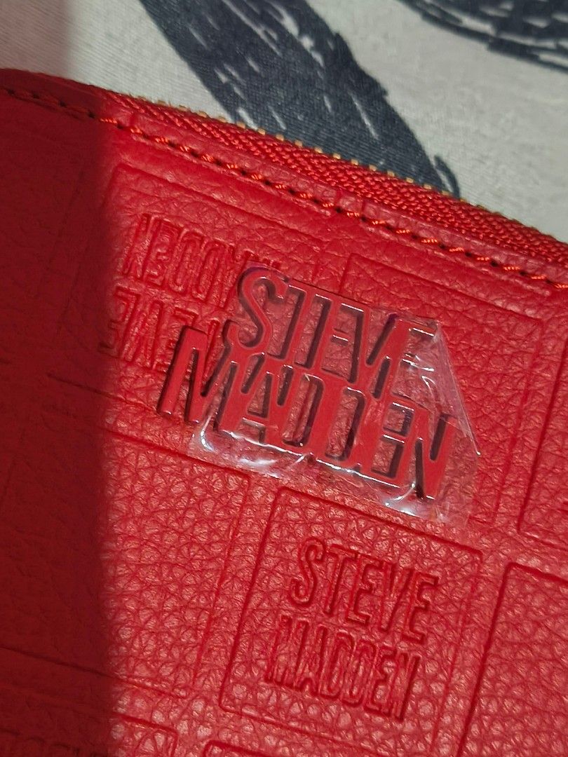 Steve Madden Red Zip Around Wallet (Category: Wallets & Card holders) located in Cavite. Submitted by mahthriftshop (Listing ID 1467382061, Image 1). Description: - Brand: Steve Madden - Color: Bright red with debossed logo grid pattern - Hardware: Gold-tone with plastic protector still on the front logo badge - Closure: Secure zip-around - Interior: Multiple card slots and spacious accordion compartments - Special Feature: Two metal rings on the