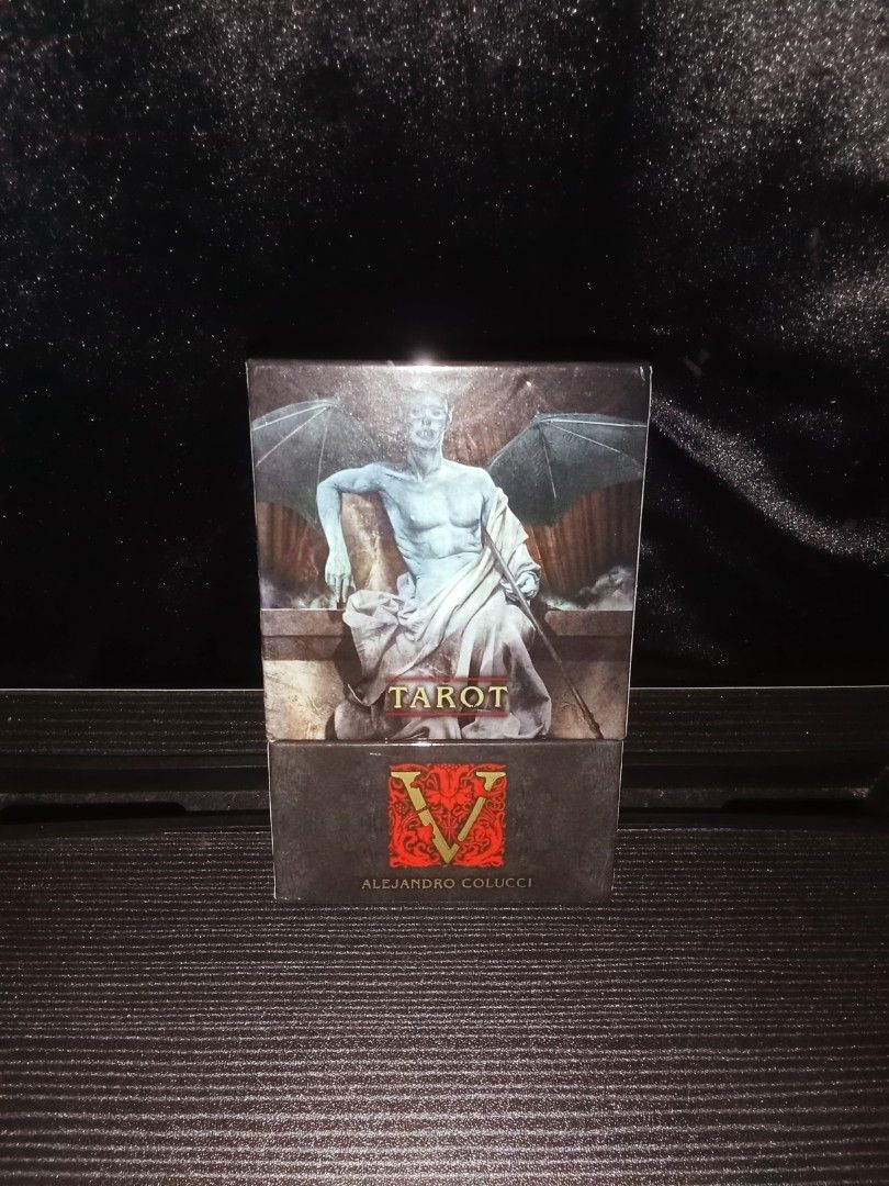 Tarot V by Alejandro Colucci (AUTHENTIC) (Category: Everything Else Others) located in Iloilo. Submitted by ya.na.06 (Listing ID 1467399519, Image 2). Description: - Authentic Alejandro Colucci Tarot deck in its original box -9.5/10 condition - Features stunning dark gothic artwork with a winged figure and intricate typography - Elegant red and gold ornate logo letter V design on the cover - Perfect collectible item for tarot readers, collectors,