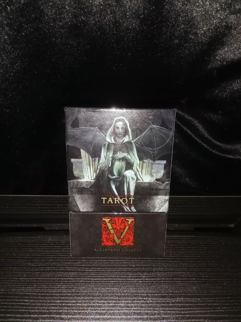 Tarot V by Alejandro Colucci (AUTHENTIC) (Category: Everything Else Others) located in Iloilo. Submitted by ya.na.06 (Listing ID 1467399519, Image 1). Description: - Authentic Alejandro Colucci Tarot deck in its original box -9.5/10 condition - Features stunning dark gothic artwork with a winged figure and intricate typography - Elegant red and gold ornate logo letter V design on the cover - Perfect collectible item for tarot readers, collectors,