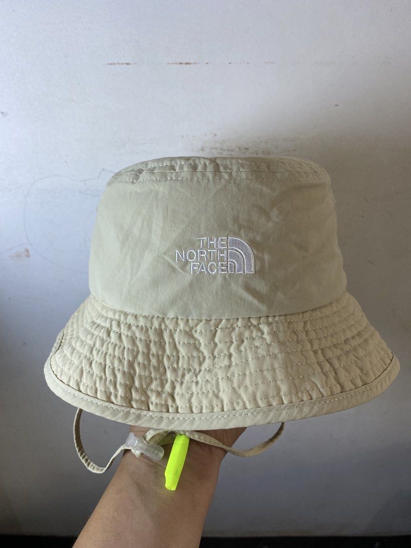 The North Face Beige Explorer Bucket Hat Size 56CM (Category: Caps & Hats) located in Manila. Submitted by kennyfranc39614 (Listing ID 1467516415, Image 1). Description: - Brand: The North Face - Color: Beige exterior with a bright yellow inner brim - Size: 56CM (marked on tag) - Fit: Adjustable toggle cord at the back for a custom fit - Extra Feature: Includes a chin strap with a detachable neon green safety whistle - Interior: Breathable mesh l