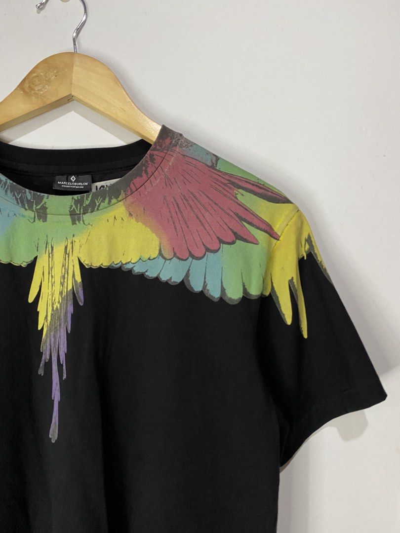 MARCELO BURLON TSHIRT (Category: Tshirts & Polo Shirts ) located in Jaen. Submitted by oshimamark58418 (Listing ID 1467527097, Image 3). Description: - Brand: Marcelo Burlon County of Milan - Color: Black with multi-color feather/wing graphic print - Size: Medium (19" width x 27" length) - Design: Iconic graphic print wrapping around the neckline (front and back) - Condition: Good, well-maintained pre-owned condition - Ideal for streetwear and ca