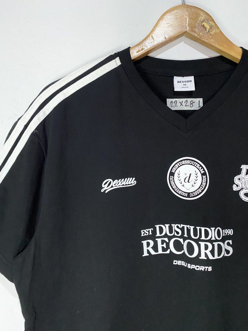 TSHIRT (Category: Tshirts & Polo Shirts ) located in Jaen. Submitted by oshimamark58418 (Listing ID 1467527341, Image 3). Description: - Brand: DESSUU - Color: Black with white prints and shoulder stripes - Size: L (Actual measurement: 22" x 28") - Neckline: V-neck - Design: Features 'DUSTUDIO 1909 RECORDS' and 'Dsu Studio' graphics on the chest - Style: Streetwear / Casual everyday tee.