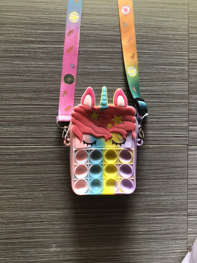 Unicorn Pop It sling bag (Category: Babies & Kids Fashion) located in Cavite. Submitted by ai__chang (Listing ID 1467405997, Image 1). Description: - Cute pastel unicorn design in vibrant rainbow shades - Built-in pop-it bubble toy on the front for endless fun - Made from durable, flexible, and easy-to-clean silicone - Long, adjustable strap featuring fun ice cream and donut prints - Perfect size for carrying small daily essentials - Great gift i