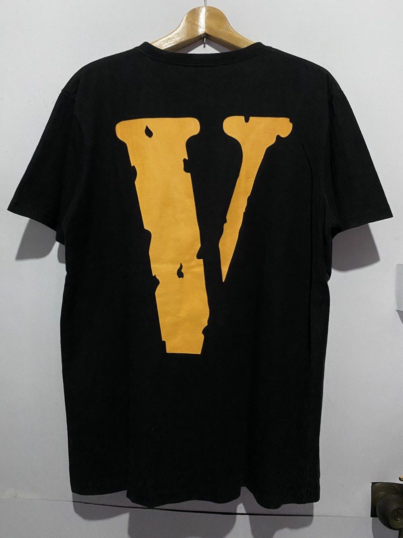 Vlone Black Tee With Yellow V Logo (Category: Tshirts & Polo Shirts ) located in Jaen. Submitted by oshimamark58418 (Listing ID 1467552431, Image 2). Description: Black Vlone t-shirt. Large yellow V graphic on the back. Front has Vlone text print in white and yellow. Tag says size M, but handwritten tape shows 21x28 L. 100% cotton material. Made in China..