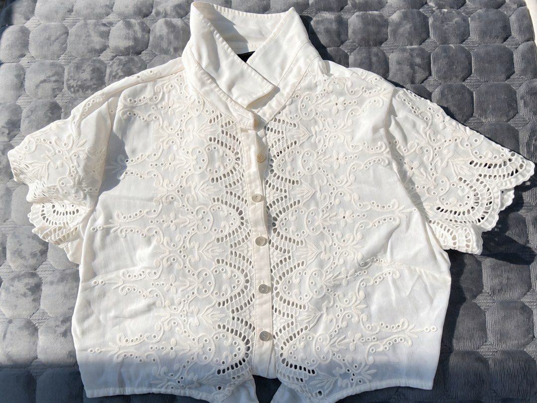 White lace embroidered short sleeve button-up blouse (Category: Blouses) located in Cabadbaran. Submitted by manualrj2491753 (Listing ID 1467498703, Image 1). Description: - Color: Classic White - Design: Button-up with intricate lace embroidery on front and sleeves - Details: High collar neckline, trendy tie-front hem, and delicate cut-out patterns - Sleeves: Short sleeves - Fabric: Lightweight and breathable - Condition: Brand new / Excellent q