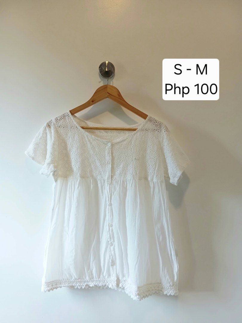 White lace trim button-up blouse top S-M (Category: Blouses) located in Antipolo. Submitted by wisecat.4a7eea (Listing ID 1467401246, Image 1). Description: - Color: White - Fit: Comfortably fits Small to Medium - Material: Lightweight gathered fabric - Design: Cut-out lace yoke and sleeves, front button closure - Details: Matching buttons and crocheted lace trim along the bottom hem - Styling: Great basic piece for warm weather, easy to pair wit