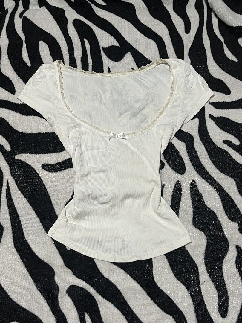 White Ribbed Scoop Neck Tee With Lace Trim (Category: Shirts) located in Manila. Submitted by y2kcloset_ (Listing ID 1467477220, Image 1). Description: - Color/Design: White ribbed short-sleeve top with delicate cream lace trim and a front satin bow - Fit: Body-hugging, fitted silhouette - Material: Super soft and comfortable ribbed cotton, perfect for daily wear - Styling: Easy to pair with jeans, shorts, or skirts - Condition: Brand new / Excel