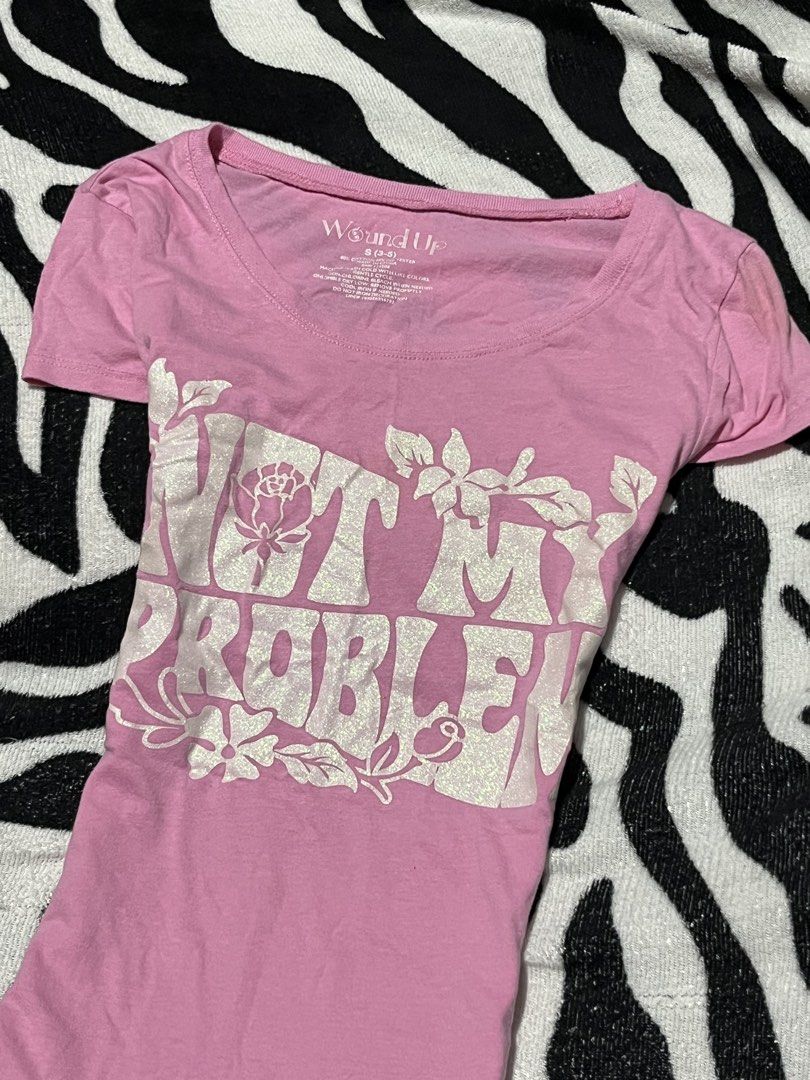 Wound Up Not My Problem Graphic Tee Pink Small (Category: Shirts) located in Manila. Submitted by y2kcloset_ (Listing ID 1467477612, Image 2). Description: - Brand/Style: Wound Up pink graphic tee with a retro vibe - Size: Small (best fits sizes 3-5) - Material: Comfortable cotton and polyester blend, machine washable - Design: Bold sparkly silver 'Not My Problem' lettering with floral line art, scoop neck, and short sleeves - Styling: Easy to pa