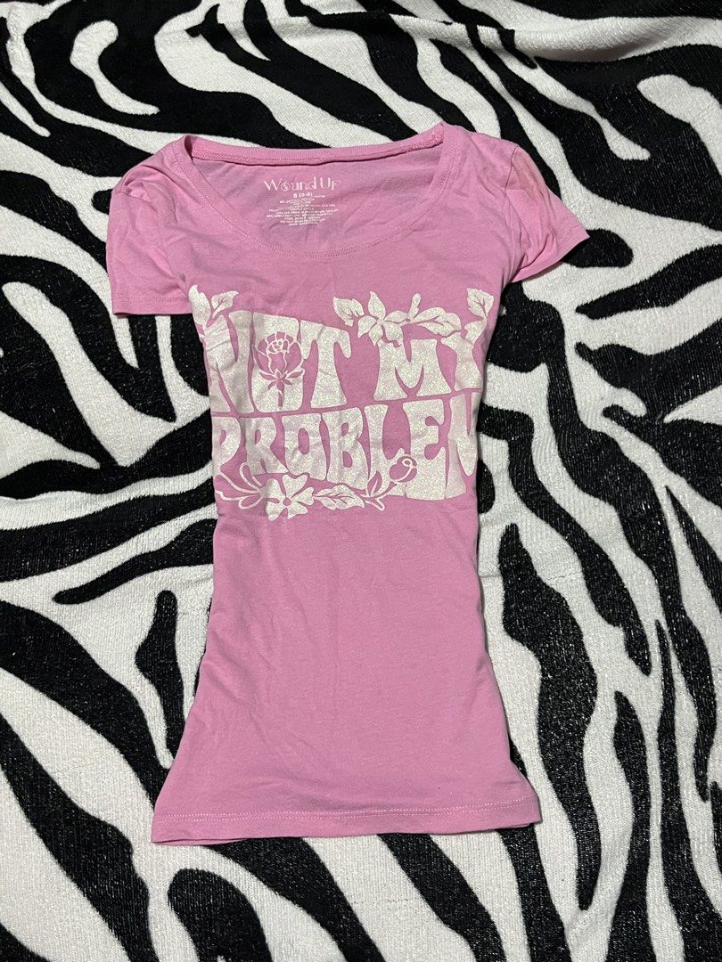 Wound Up Not My Problem Graphic Tee Pink Small (Category: Shirts) located in Manila. Submitted by y2kcloset_ (Listing ID 1467477612, Image 1). Description: - Brand/Style: Wound Up pink graphic tee with a retro vibe - Size: Small (best fits sizes 3-5) - Material: Comfortable cotton and polyester blend, machine washable - Design: Bold sparkly silver 'Not My Problem' lettering with floral line art, scoop neck, and short sleeves - Styling: Easy to pa