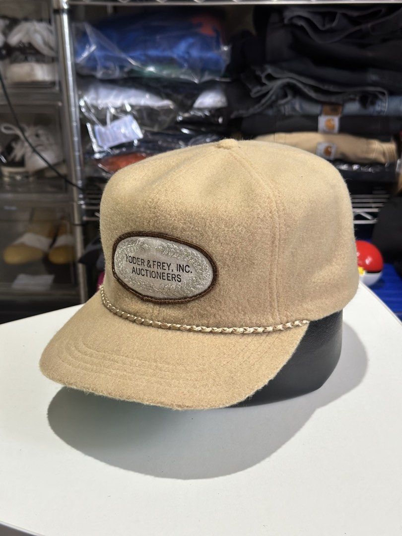 Yoder & Frey Inc. Auctioneers Wool Cap (Category: Caps & Hats) located in Daet. Submitted by thrifthings2018 (Listing ID 1467446471, Image 3). Description: - Color: Tan wool with a green underbrim - Design: Structured crown, flat brim, and braided cord trim - Patch: Embroidered Yoder & Frey, Inc. Auctioneers logo on the front - Comfort: Dri-N-Cool interior sweatband - Fit: Adjustable strap closure with gold-tone hardware - Condition: Clean and re