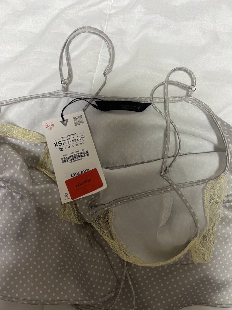 ZARA Polka Dot Satin Camisole Top (Category: Sleeveless) located in Cebu City. Submitted by declutteringloved (Listing ID 1467572467, Image 3). Description: - Brand: Zara - Size: XS - Condition: Brand new with original retail tags attached - Color/Pattern: Grey with white polka dots - Material/Finish: Elegant satin - Details: Lace-trimmed V-neckline, front button placket, and waist drawstring tie - Straps: Adjustable spaghetti straps.