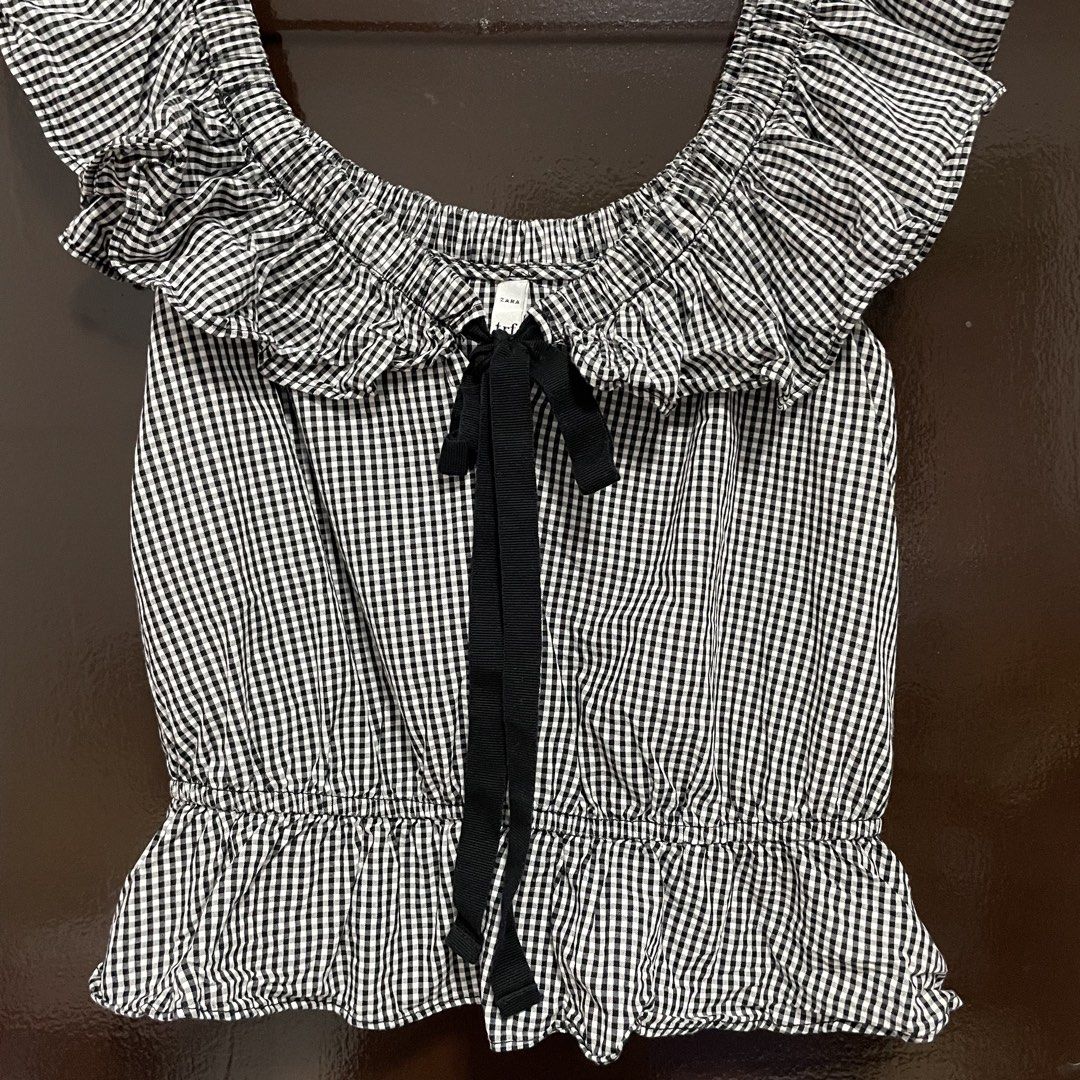 Zara TRF Black and White Gingham Ruffle Blouse (Category: Blouses) located in Pasay City. Submitted by lovedbyzea (Listing ID 1467526234, Image 2). Description: - Style: Classic black and white gingham check pattern - Fit: Size XS (EUR, USA, MEX) - Details: Elasticated neckline, ruffle sleeves, and front black ribbon tie closure - Silhouette: Peplum hem with a gathered waist - Material: Lightweight cotton fabric - Origin: Made in Morocco.