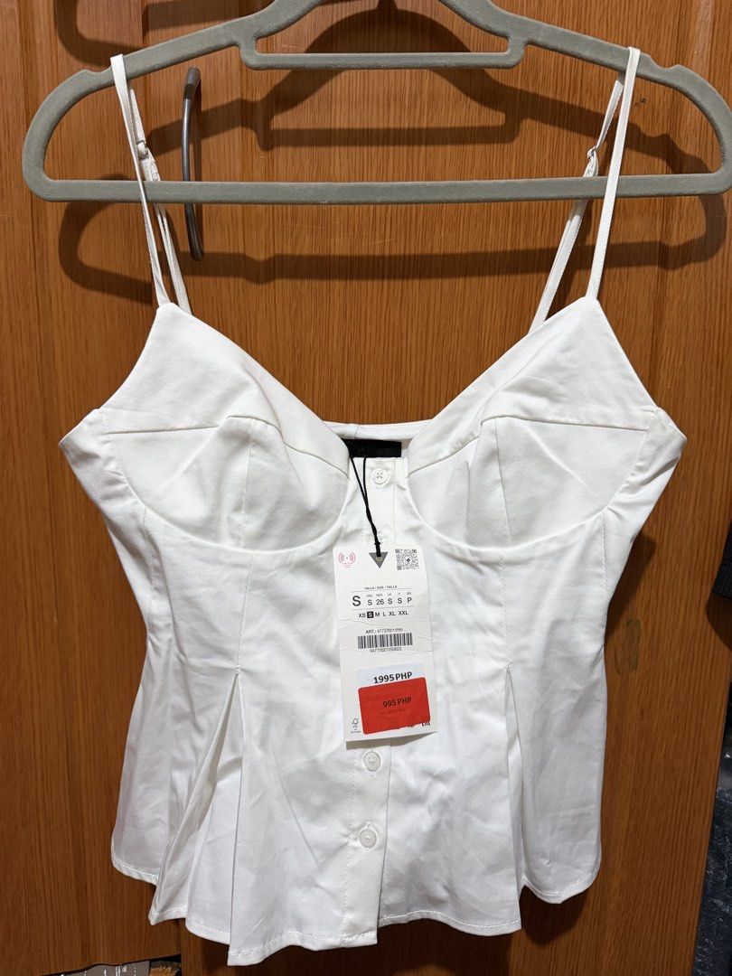 Zara White Corset Style Spaghetti Strap Top (Category: Sleeveless) located in Muntinlupa City. Submitted by biancaagbscloset (Listing ID 1467513352, Image 1). Description: - Style: White spaghetti strap top with bustier cups and front button closure - Design: Pleated waist flare for a flattering shape - Size: S - Condition: Brand new with original tags attached, never worn - Versatility: Great for casual days or nights out.