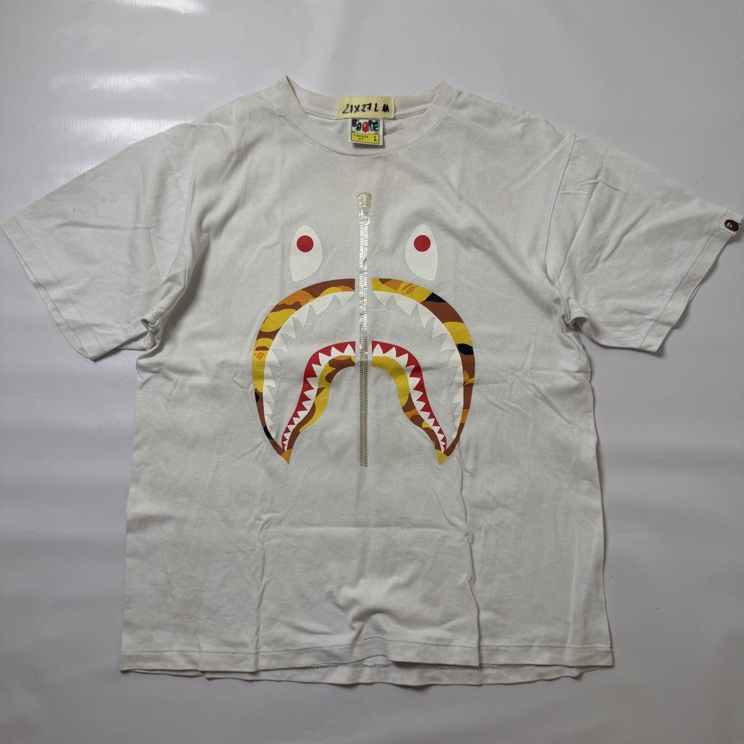 A Bathing Ape BAPE Shark White Tee (Category: Tshirts & Polo Shirts ) located in Gapan. Submitted by rasthriftshop (Listing ID 1467797084, Image 1). Description: BAPE Size on tag: L Dimes: 21 x 27 ₱950 + sf Condition: Excellent Color rate: 9/10 Issue: None.